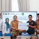 Kepala Dinas PMD Tanah Bumbu menyerahkan bantuan simbolis kepada ahli waris peserta BPJS Ketenagakerjaan yang mengalami kecelakaan kerja, didampingi Kepala BPJS Ketenagakerjaan Batulicin dan Camat Kusan Hilir