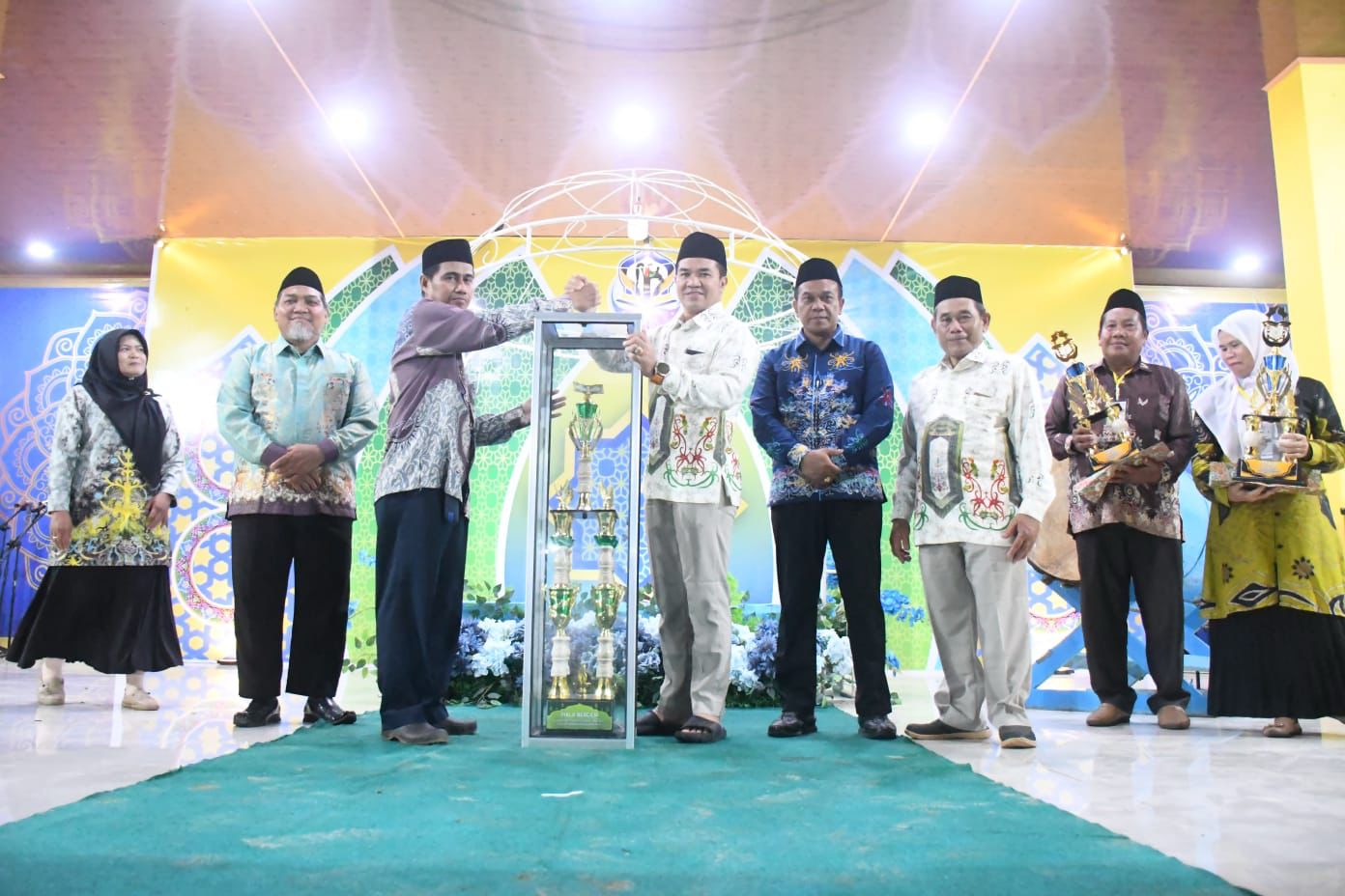 Bupati Pulang Pisau H. Ahmad Rifa’i menyerahkan piala kepada kafilah Kecamatan Kahayan Hilir sebagai juara umum MTQH XIII 2025, disambut sorak meriah peserta dan masyarakat.