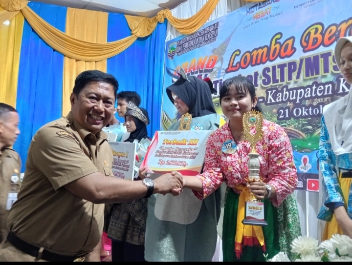 Kepala Dinas Perpustakaan Kotabaru menyerahkan trofi kepada Siti Nurhayatul Hasanah, pemenang Juara 1 Lomba Bercerita SMP/MTs se-Kabupaten Kotabaru 2025.