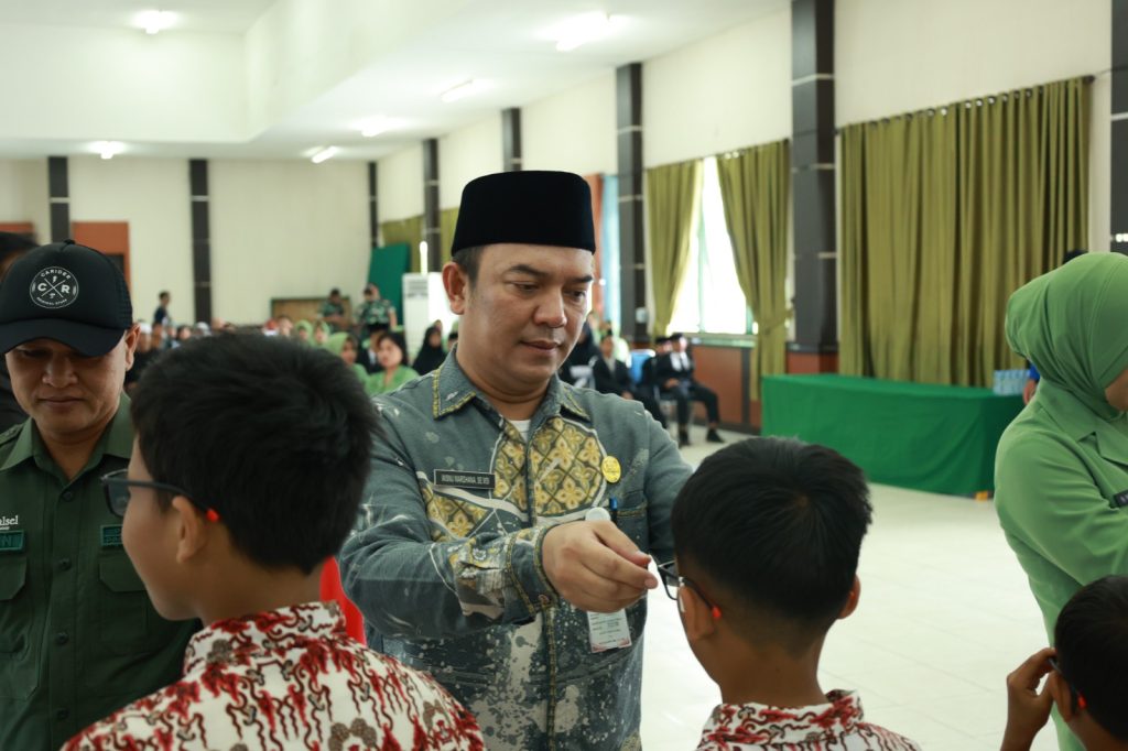 Plt. Asisten Pemerintahan dan Kesra Tanah Bumbu, M. Putu Wisnu Wardhana, mewakili Bupati menyerahkan kacamata gratis kepada salah satu siswa dalam kegiatan bakti sosial HUT ke-80 TNI di Aula Kodim 1022/Tanah Bumbu.
