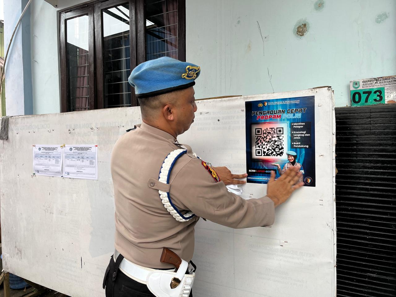 Personel Polres Hulu Sungai Utara memasang stiker QR Code pengaduan Propam Polri di papan informasi Kantor Kelurahan Antasari, Amuntai Tengah.