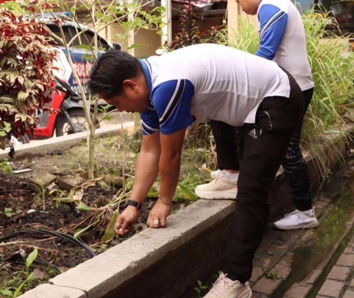 Anggota Polres Batola membersihkan sampah dan rumput di tepi saluran air dalam kegiatan bersih-bersih lingkungan Jumat Berkah.