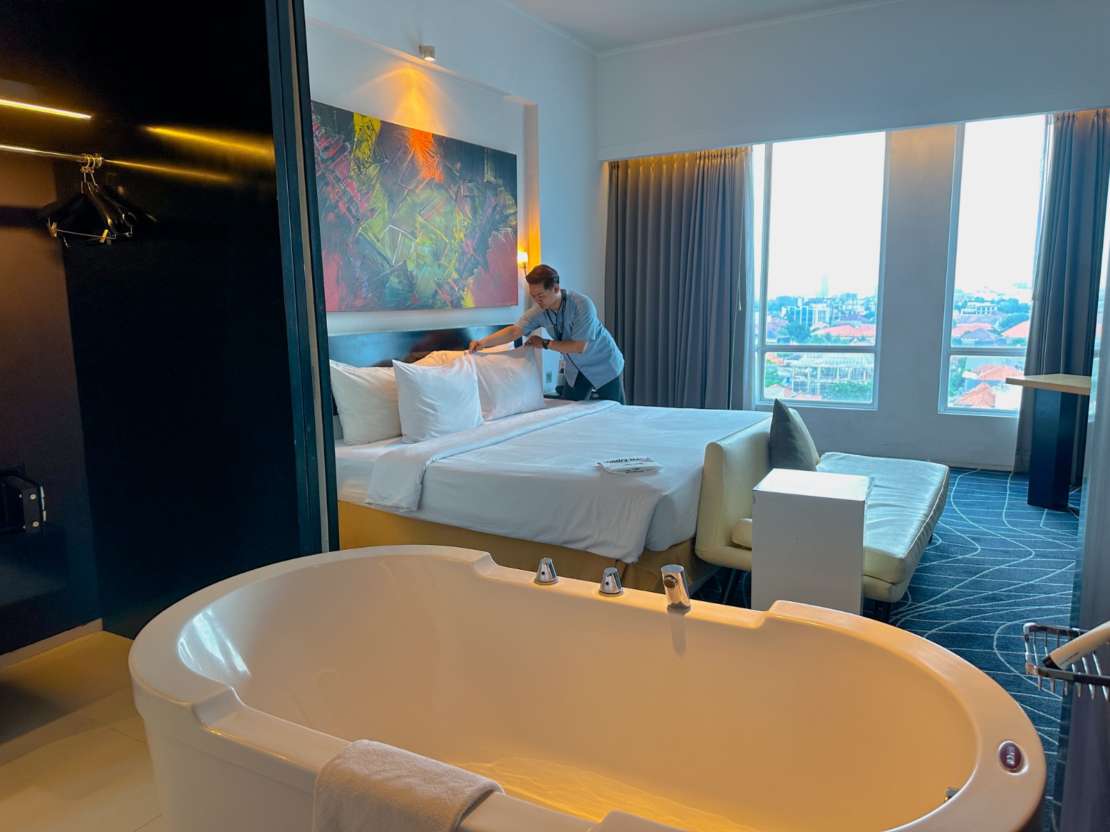 Kamar hotel ARTOTEL TS Suites Surabaya dengan desain luas, dilengkapi bathtub, tempat tidur besar, dan pemandangan kota untuk staycation Lebaran.