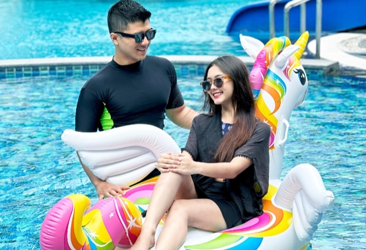 Pria dan wanita bersantai di kolam renang menggunakan pelampung unicorn warna-warni, menikmati suasana liburan di area waterpark.