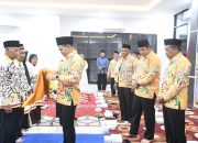 Bupati Pulang Pisau menyerahkan perlengkapan kepada jemaah haji dalam acara pelepasan keberangkatan haji tahun 2026 di dalam ruangan.