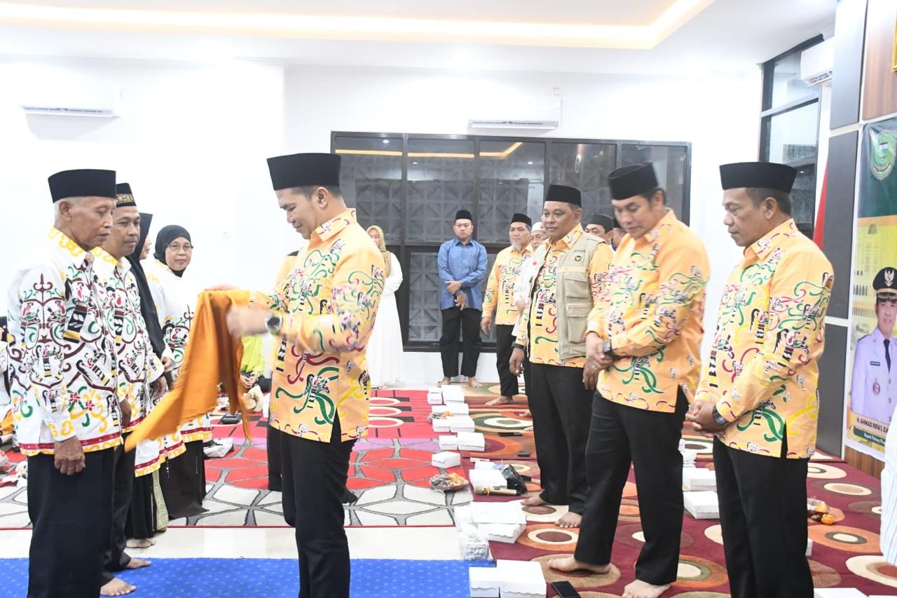 Bupati Pulang Pisau menyerahkan perlengkapan kepada jemaah haji dalam acara pelepasan keberangkatan haji tahun 2026 di dalam ruangan.