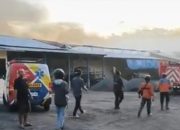 Petugas damkar dan warga di lokasi kebakaran gudang pabrik rokok di Buring Malang dengan asap tebal membumbung dari bangunan.