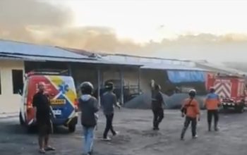 Petugas damkar dan warga di lokasi kebakaran gudang pabrik rokok di Buring Malang dengan asap tebal membumbung dari bangunan.