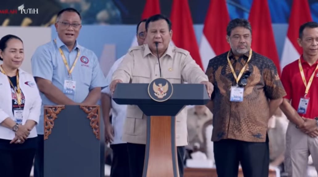Presiden Prabowo Subianto berpidato di podium pada peringatan Hari Buruh 2026 di Monas, Jakarta, didampingi sejumlah pejabat dan perwakilan buruh.