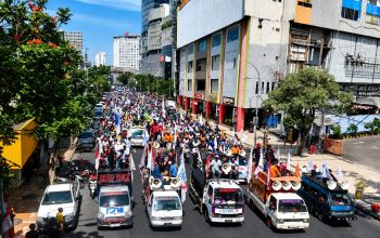 Ribuan buruh berkonvoi menggunakan kendaraan dan membawa spanduk saat aksi Hari Buruh Internasional 2026 di Surabaya.