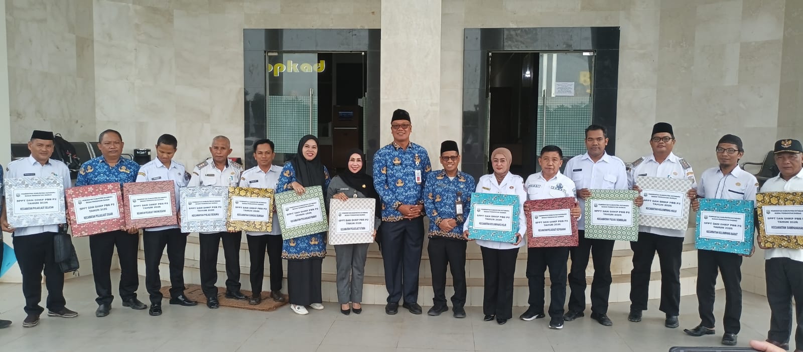 Kepala Bapenda Kotabaru bersama jajaran dan perwakilan kecamatan berfoto sambil memegang dokumen SPPT PBB-P2 Tahun 2026 di depan kantor pemerintahan.