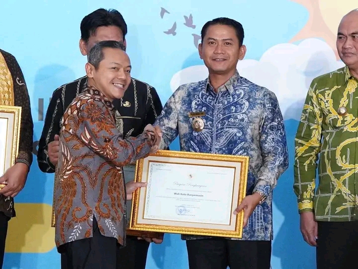 Wali Kota Banjarmasin memegang piagam penghargaan revitalisasi bahasa daerah di atas panggung.