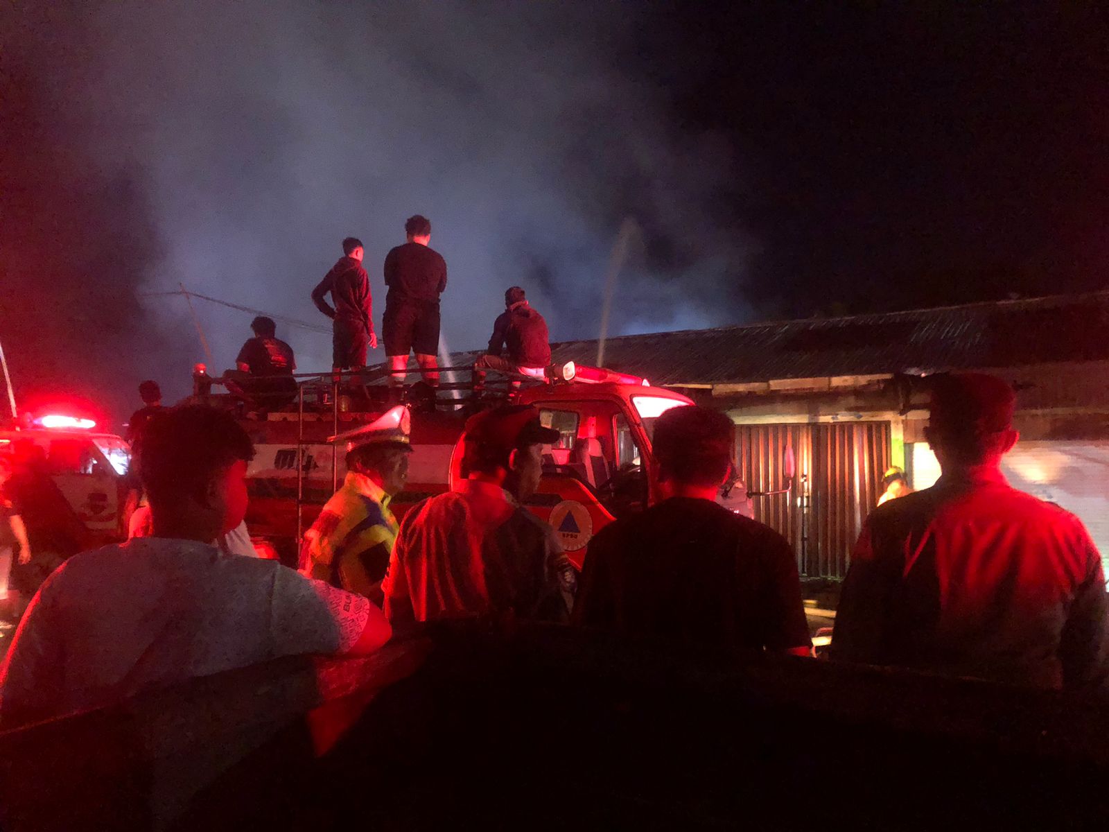 Petugas damkar menyemprotkan air ke bangunan kontrakan yang terbakar.