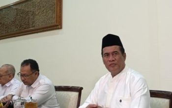 Menteri Pertanian dan Kepala Badan Pangan Nasional, Amran Sulaiman, mengenakan baju putih dan peci hitam saat menghadiri pertemuan resmi membahas sektor pertanian dan ketahanan pangan nasional.
