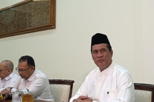 Menteri Pertanian dan Kepala Badan Pangan Nasional, Amran Sulaiman, mengenakan baju putih dan peci hitam saat menghadiri pertemuan resmi membahas sektor pertanian dan ketahanan pangan nasional.