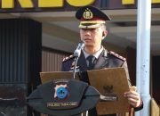 Polisi berpangkat di podium membacakan teks, peserta upacara baris rapi di belakang