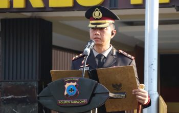Polisi berpangkat di podium membacakan teks, peserta upacara baris rapi di belakang