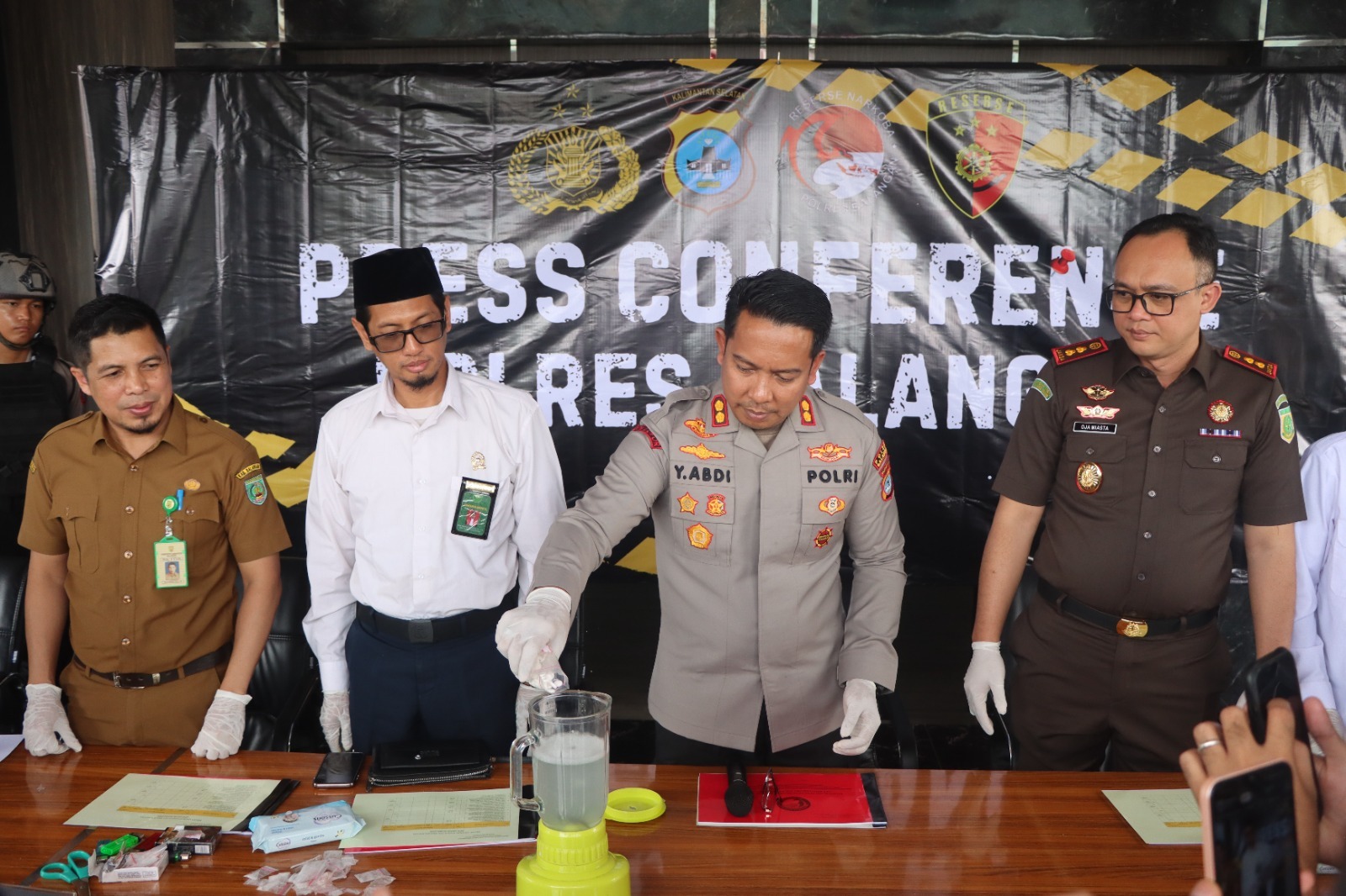 Petugas menuangkan bubuk dan butiran obat ke dalam blender, polisi lain melihat