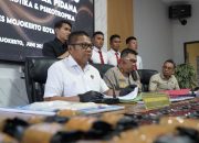 Tiga polisi duduk di meja konferensi pers, latar spanduk biru Ditresnarkoba Polda Jatim