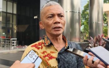 Pria berpakaian batik bicara di depan wartawan