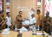Empat orang berjabat tangan di depan piagam penghargaan