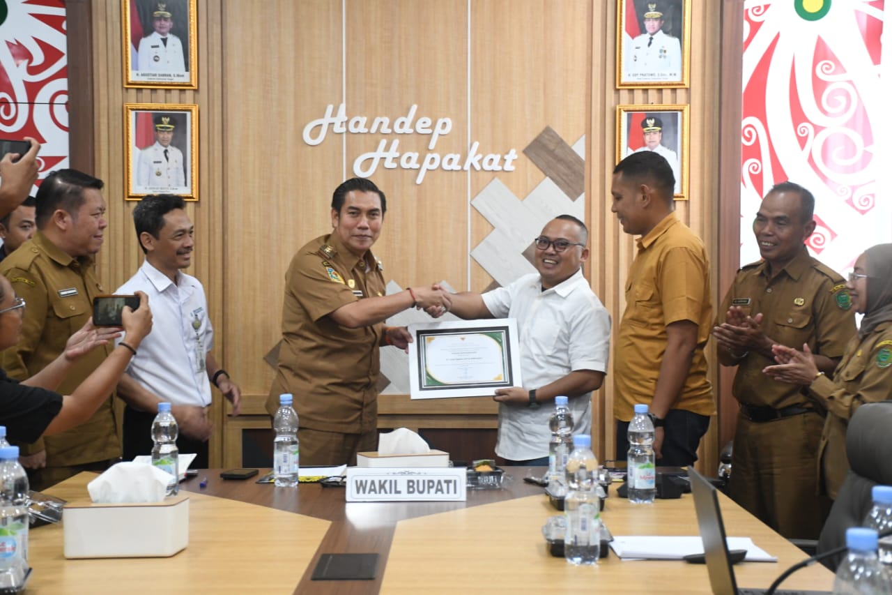 Empat orang berjabat tangan di depan piagam penghargaan