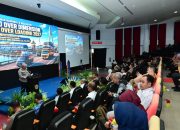 Tiga orang duduk di meja panelis, latar spanduk seminar