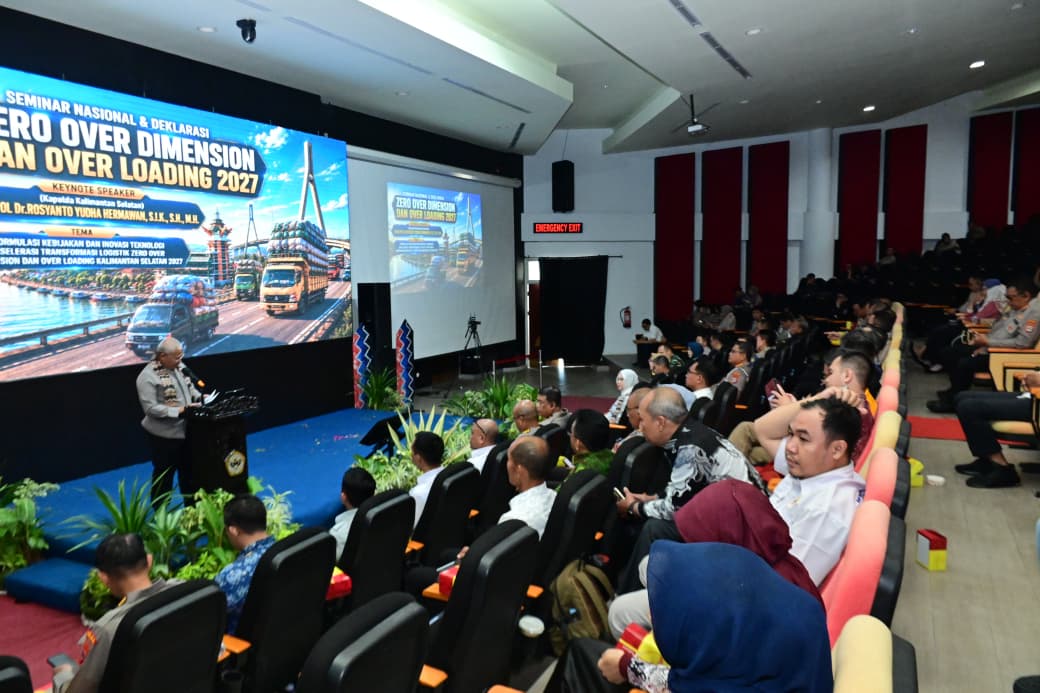 Tiga orang duduk di meja panelis, latar spanduk seminar
