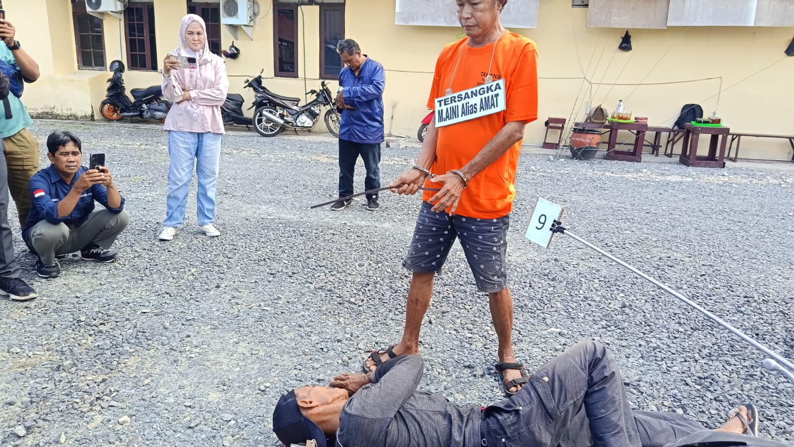 Tersangka berbaju tahanan menunjuk ke suatu titik di lokasi