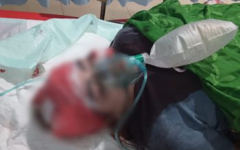 Perempuan terbaring di tempat tidur rumah sakit, petugas medis di sampingnya